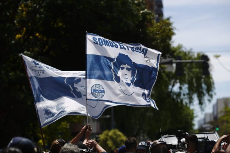 OLIVOS, ARGENTINA - NOVEMBER 04: People wave flags with the image of Diego Maradona outside the Clínica Olivos on November 4, 2020 in Olivos, Argentina. Former football star Diego Maradona recovers in hospital after undergoing a surgery for a clot in his brain on Tuesday. He had been admitted to hospital a day before with symptoms of anemia and dehydration. (Photo by Marcos Brindicci/Getty Images)