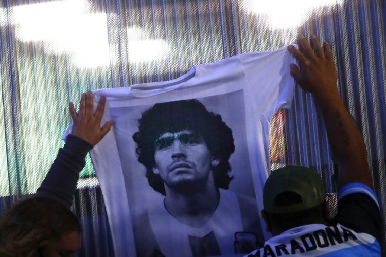 OLIVOS, ARGENTINA - NOVEMBER 03: Fans hold a jersey with the face of Diego Maradona at Clínica Olivos on November 03, 2020 in Olivos, Argentina. Personal doctor of Maradona, Leopoldo Luque, confirmed the former footballer will under a surgery to treat a clot in his brain. Maradona, who turned 60 on Friday 30, had spent the night of Monday hospitalized after being admitted with symptoms of depression. (Photo by Marcos Brindicci/Getty Images)