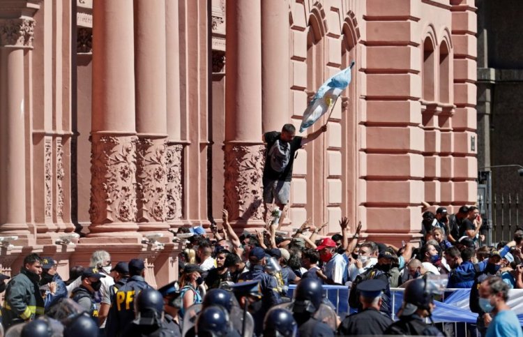 A fan climbing on the facade of the Casa Rosada government house, holds up an Argentinian flag as he waits to enter to pay tribute to Argentinian late football legend Diego Armando Maradona, in Buenos Aires, on November 26, 2020. - Argentine football legend Diego Maradona will be buried Thursday on the outskirts of Buenos Aires, a spokesman said. Maradona, who died of a heart attack Wednesday at the age of 60, will be laid to rest in the Jardin de Paz cemetery, where his parents were also buried, Sebastian Sanchi told AFP. (Photo by ALEJANDRO PAGNI / AFP) (Photo by ALEJANDRO PAGNI/AFP via Getty Images)